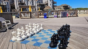 A large chessboard set up on a wooden deck with a view of beach houses in the background.