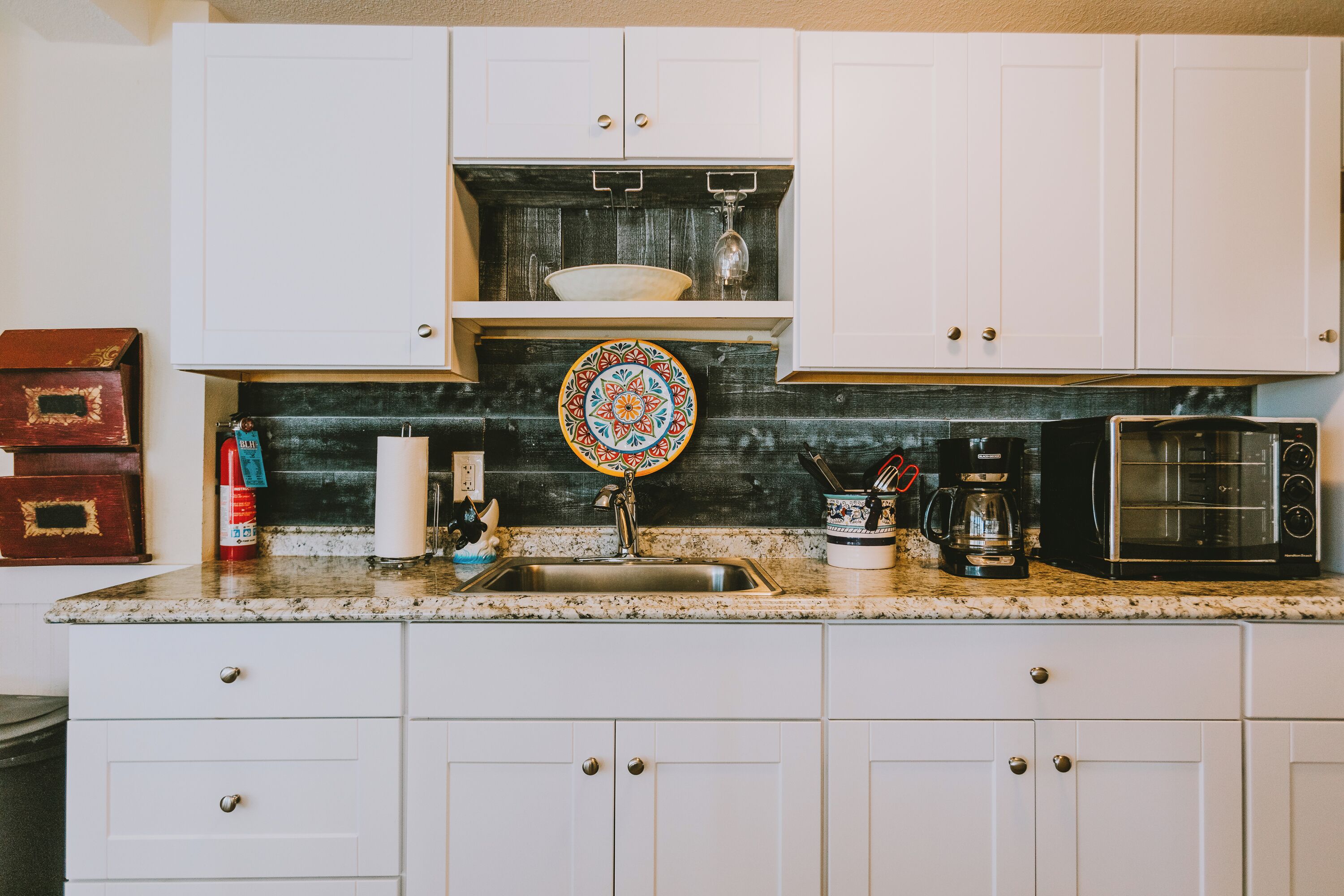 A kitchen with white cabinets, a granite countertop, a coffee maker, and a microwave.