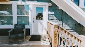A wooden deck with a bench, a white door with a glass panel, and a wooden staircase with a railing.
