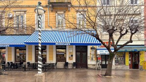 Un restaurant McDonald's avec une terrasse, un arbre et un magasin de tabac en arrière-plan.