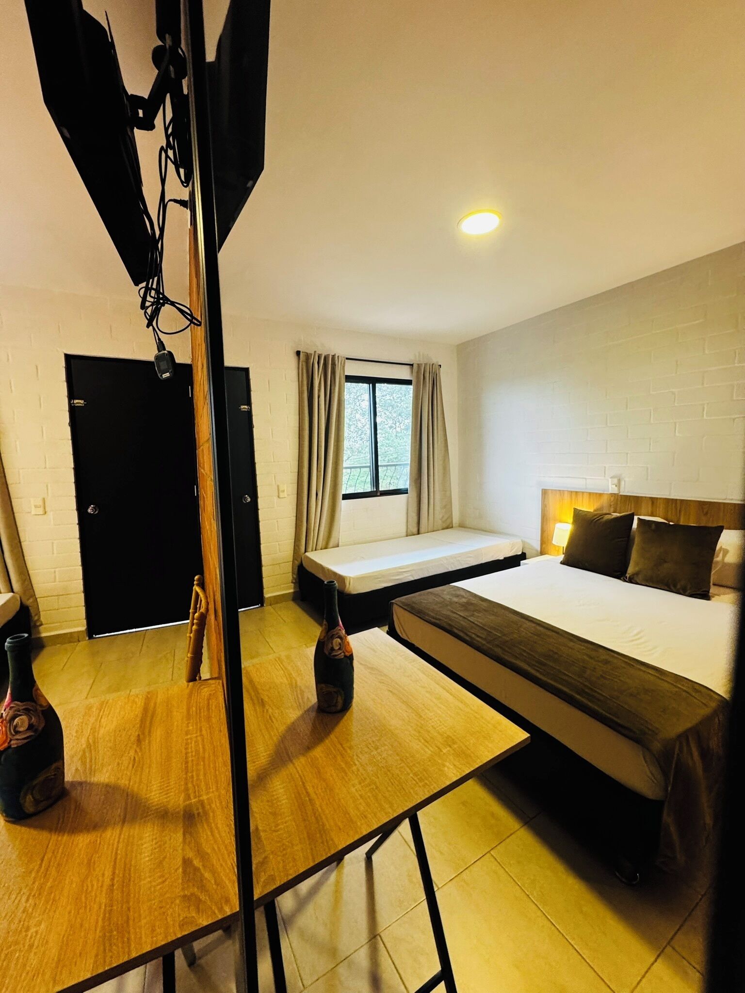 A hotel room with a bed, a sofa, a small table, a window with curtains, and a door.