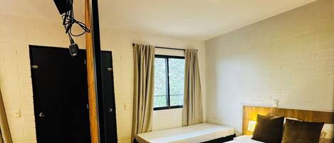 A hotel room with a bed, a sofa, a small table, a window with curtains, and a door.