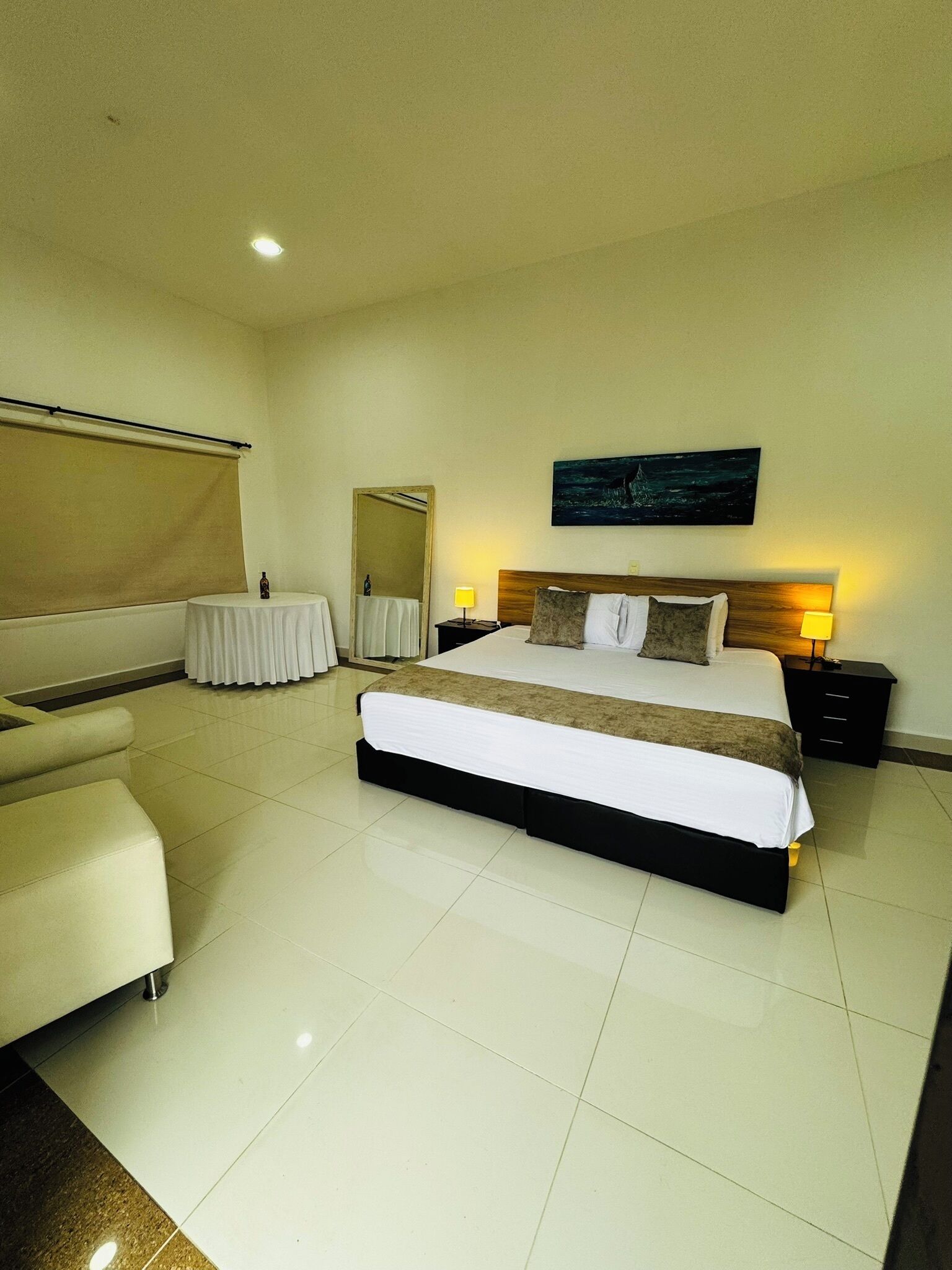 A hotel room with a large bed, a bedside table, a small round table, a sofa, and a large mirror.