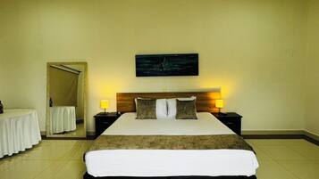 A hotel room with a large bed, a bedside table, a nightstand, a mirror, and a painting on the wall.
