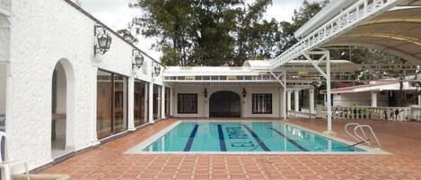 A swimming pool with a white building on one side and a covered area on the other.