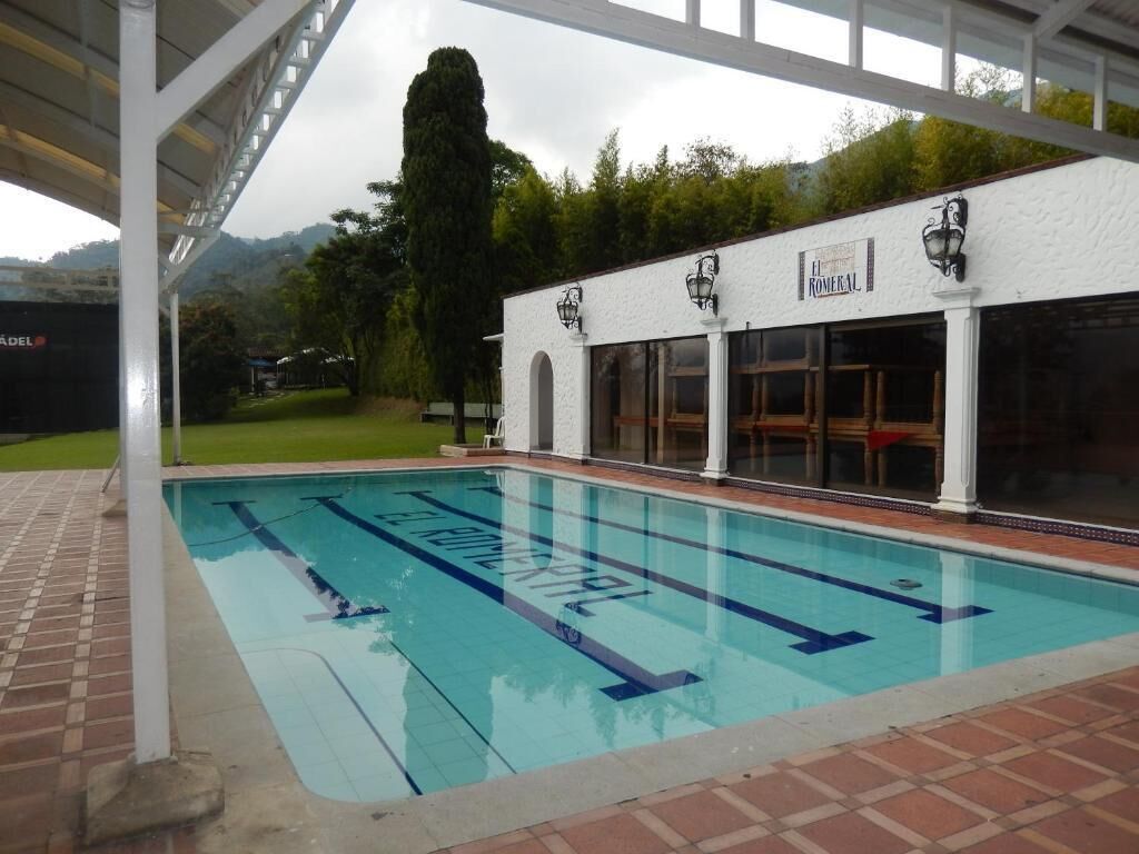 A swimming pool with clear lane markings, a covered seating area, and a building with a sign that reads 'El Romerol.'