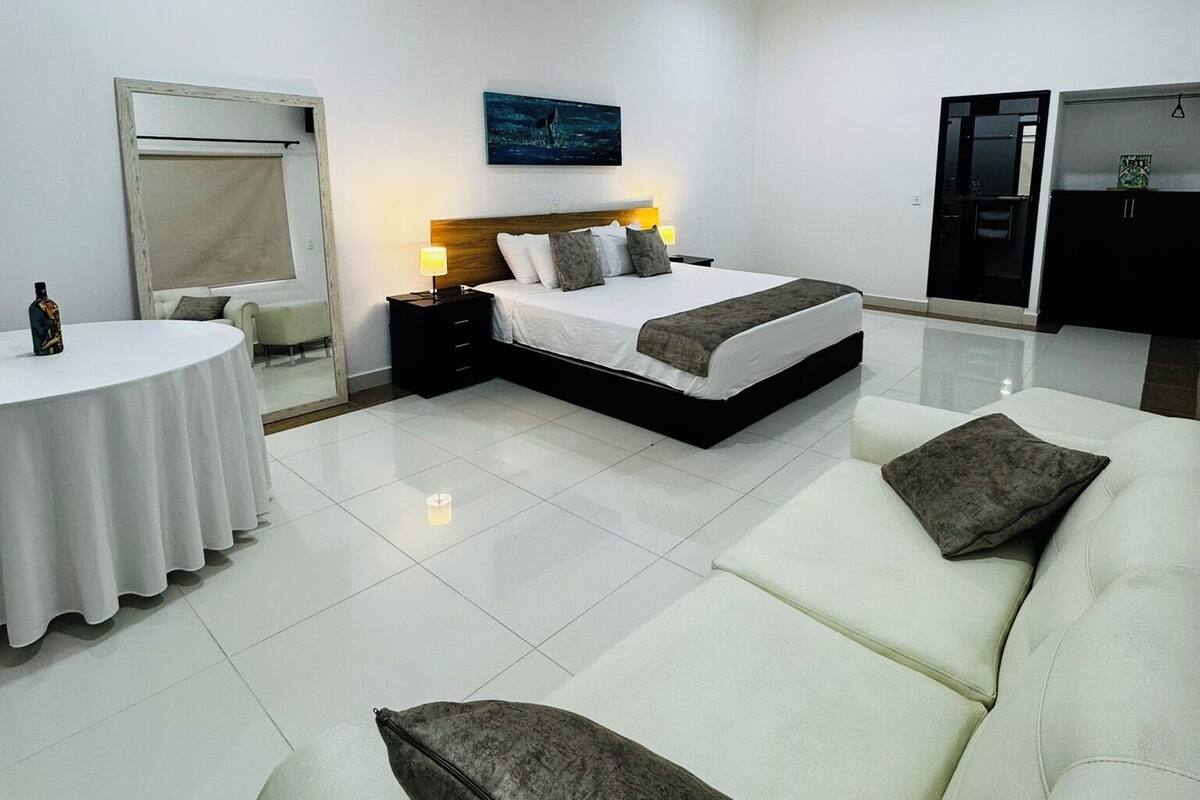 A modern bedroom with a bed, a sofa, a round table, and a mirror.