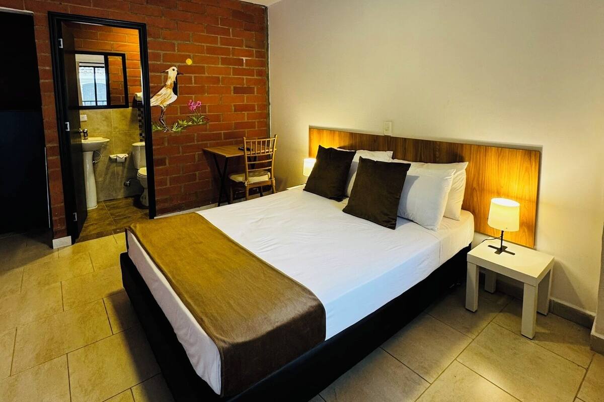A modern hotel room with a large bed, a wooden headboard, a nightstand, and a small desk with a chair.