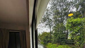 Ein Hotelzimmer mit Bett, Stuhl und Tisch. Durch das Fenster ist eine Straße und Grünfläche zu sehen.