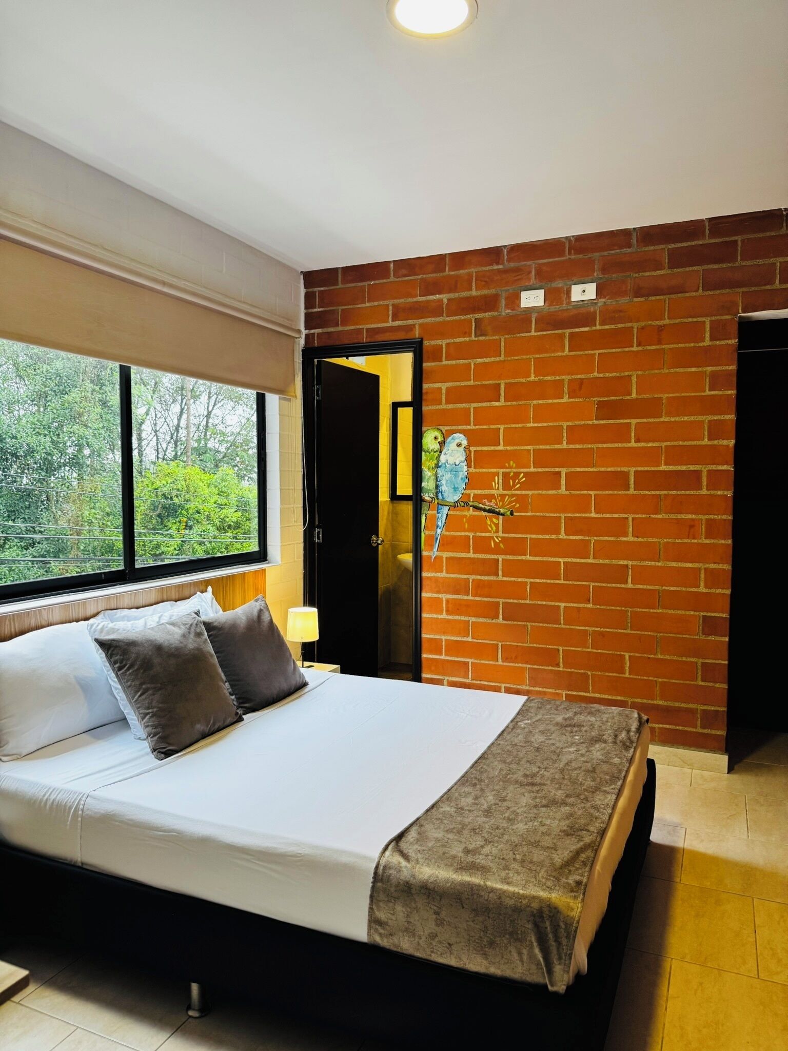 Une chambre avec un grand lit, un mur en briques et une fenêtre donnant sur des arbres.
