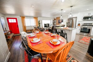 Een moderne keuken met roestvrijstalen apparatuur, een eethoek met een houten tafel en stoelen, en een rode deur.