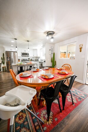 A modern kitchen with stainless steel appliances, a dining area with a wooden table and chairs, and a red patterned rug. - Arvada Getaway | Hot Tub | Fire Pit | Light Rail (Arvada)