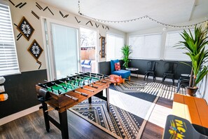 A room with a foosball table, a blue sofa, a patterned rug, and a potted plant. - Arvada Getaway | Hot Tub | Fire Pit | Light Rail (Arvada)