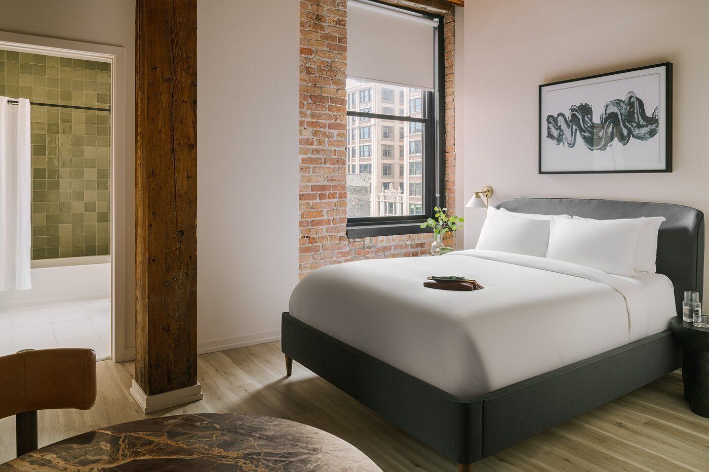 A modern hotel room with a large bed, a view of the city through a window, and a minimalist decor.