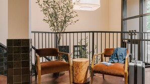 A lobby with two brown leather chairs, a marble table, and a large potted plant. - LIVN - West Loop Chicago (Chicago)