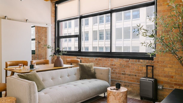 A cozy room with a sofa, a dining table, and a window with a view of buildings. - LIVN - West Loop Chicago (Chicago)