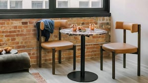 A cozy seating area with a round table and two chairs, a brick wall, and a window with a view of buildings. - LIVN - West Loop Chicago (Chicago)