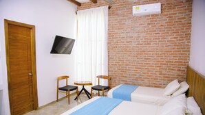 A hotel room with two beds, a TV mounted on the wall, a brick-patterned wall, and a wooden door. - Hotel Palmas del Rio Mompox (Mompos)
