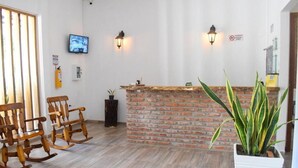 A reception area with a brick counter, wooden rocking chairs, and a potted plant. - Hotel Palmas del Rio Mompox (Mompos)