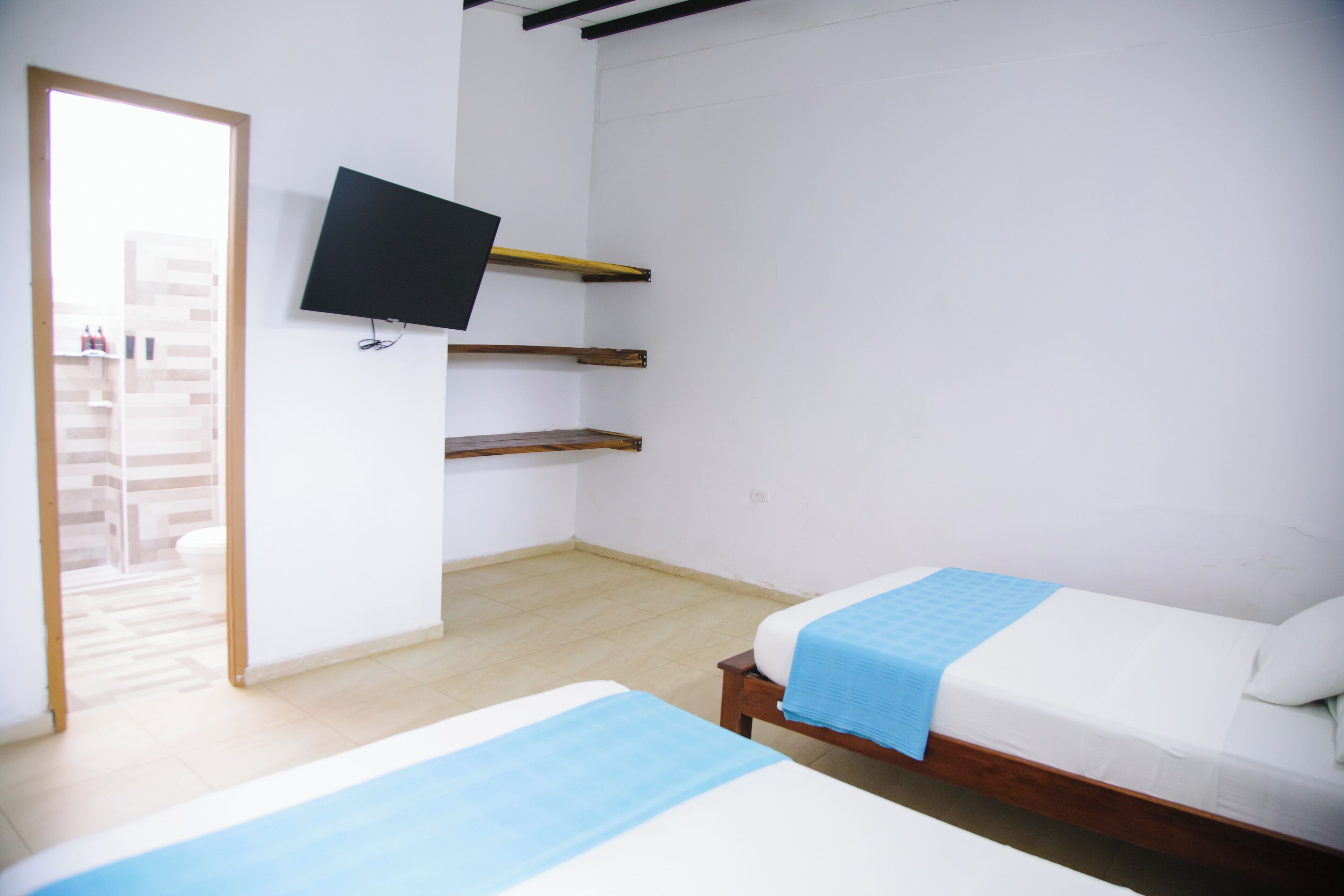 A small, clean room with two beds, a TV, and a wooden shelf.