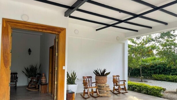 A covered outdoor area with a wooden door leading inside, a tiled floor, and two rocking chairs with potted plants. - Hotel Palmas del Rio Mompox (Mompos)