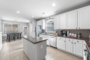 A modern kitchen with white cabinets, a central island, and a dining area with a table and chairs. - Fabulous Woodlands Home w/pool (Conroe)