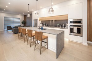 A modern kitchen with a central island, bar stools, stainless steel appliances, and pendant lighting. - Top 1% Luxury YYC |  New Build | Mins to DT (Calgary)