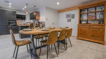Una cocina moderna con armarios oscuros, una mesa de comedor de madera preparada para seis personas, y un aparador de madera con cristalería.