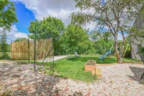 Un espacio al aire libre cercado con césped, una estructura de madera para juegos y un tobogán.