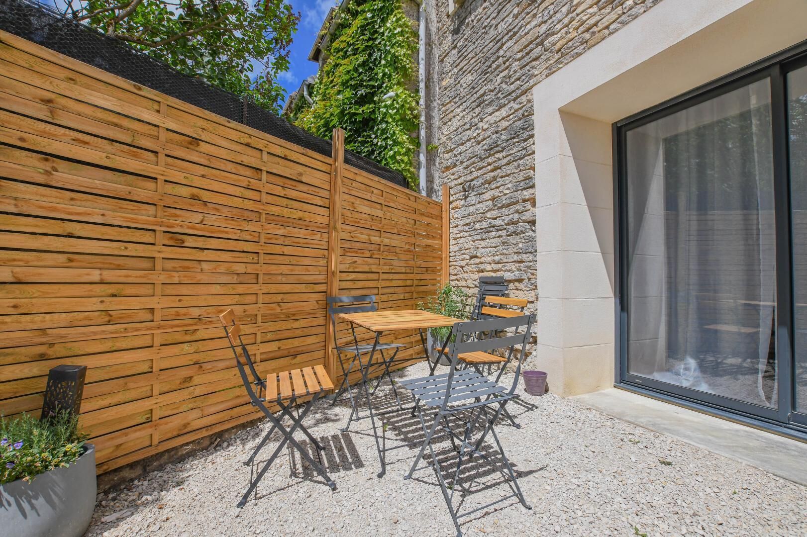A patio with a wooden fence, a table with chairs, and a stone wall.