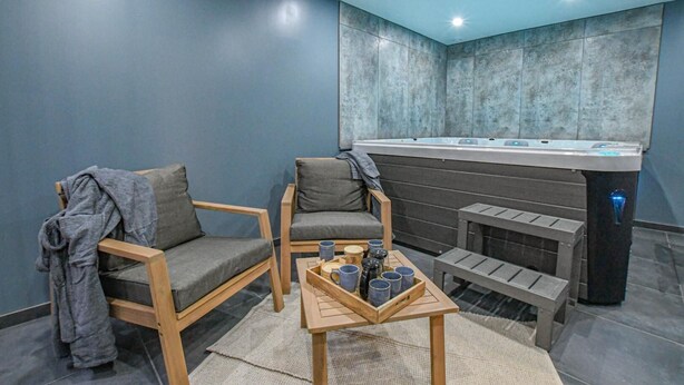 Una habitación moderna con dos sillas de madera, una mesita con tazas y una bañera grande con hidromasaje.