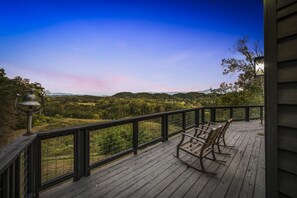 Eine Holzdielen-Terrasse mit Geländer, mit Blick auf eine bewaldete Landschaft und Hügel in der Ferne.
