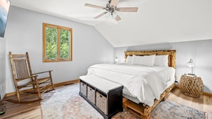 A bedroom with a sloped ceiling, a bed with a wooden headboard, a rocking chair, a small table, and a window with a view of greenery. - High Top: AMAZING views on a private 100 acres within city limits: EXCLUSIVE! (Sevierville)