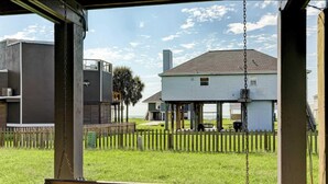 Een veranda met een schommel, een houten omheining en een wit huis op de achtergrond.
