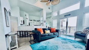 Een ruime woonkamer met een donkerblauwe bank, een vloerkleed met blauw patroon en een balkon met rieten meubilair.