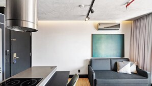 A modern kitchen with a built-in stove, a black chair, and a grey sofa with cushions. - 1811 Mercure (São Paulo)