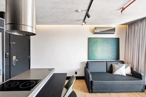 A modern kitchen with a built-in stove, a black chair, and a grey sofa with cushions. - 1811 Mercure (São Paulo)