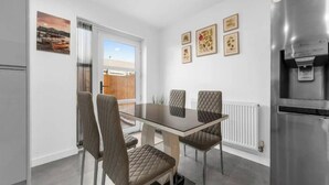 Una cocina moderna con una mesa de comedor de vidrio, cuatro sillas acolchadas, un refrigerador y una ventana con vistas al exterior.