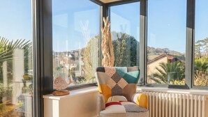 A corner room with a large window, a radiator, and a chair with patterned cushions. - Devona (Seaton)