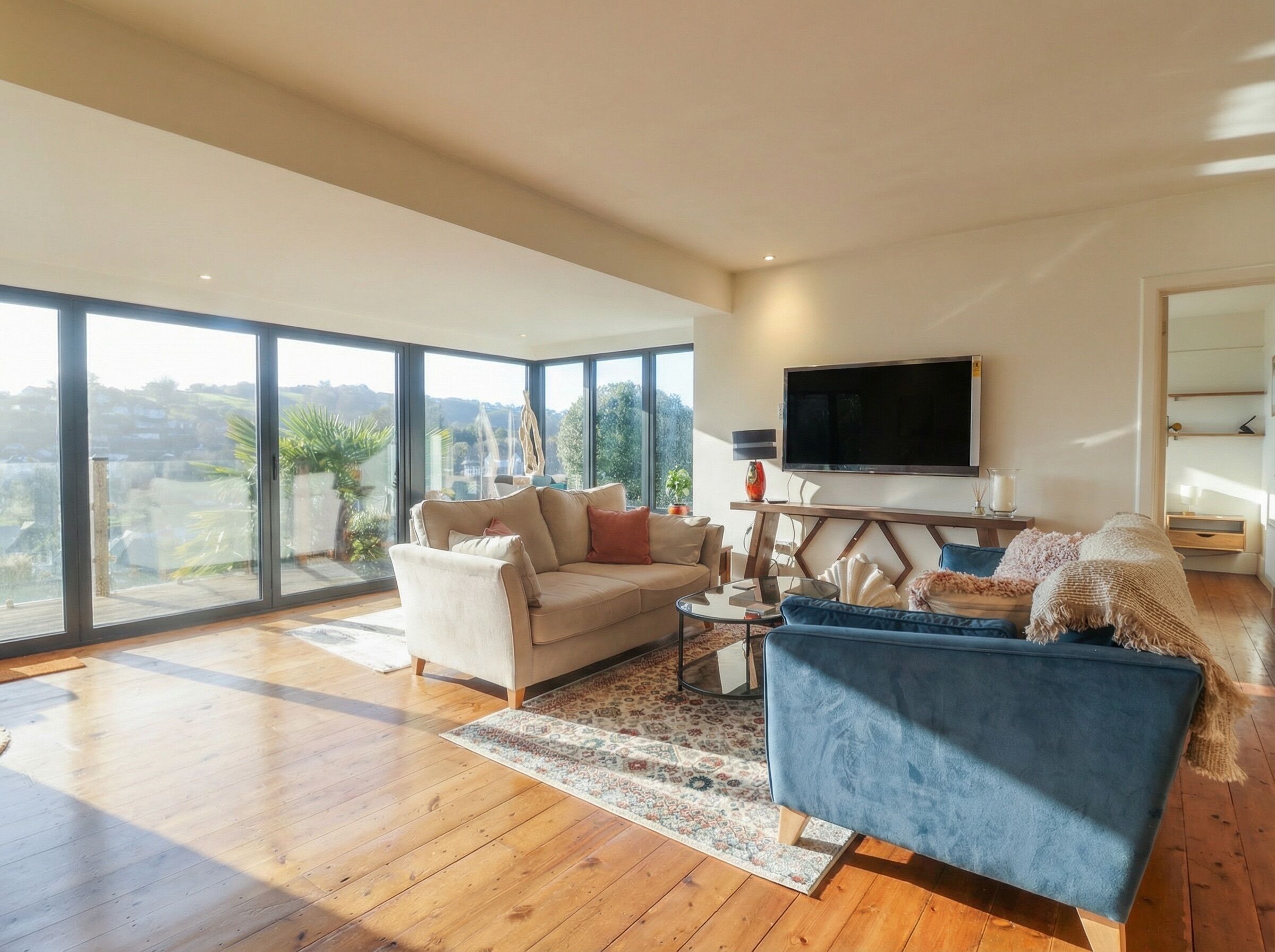 A spacious living room with a large window, a flat-screen TV, and a blue sofa.