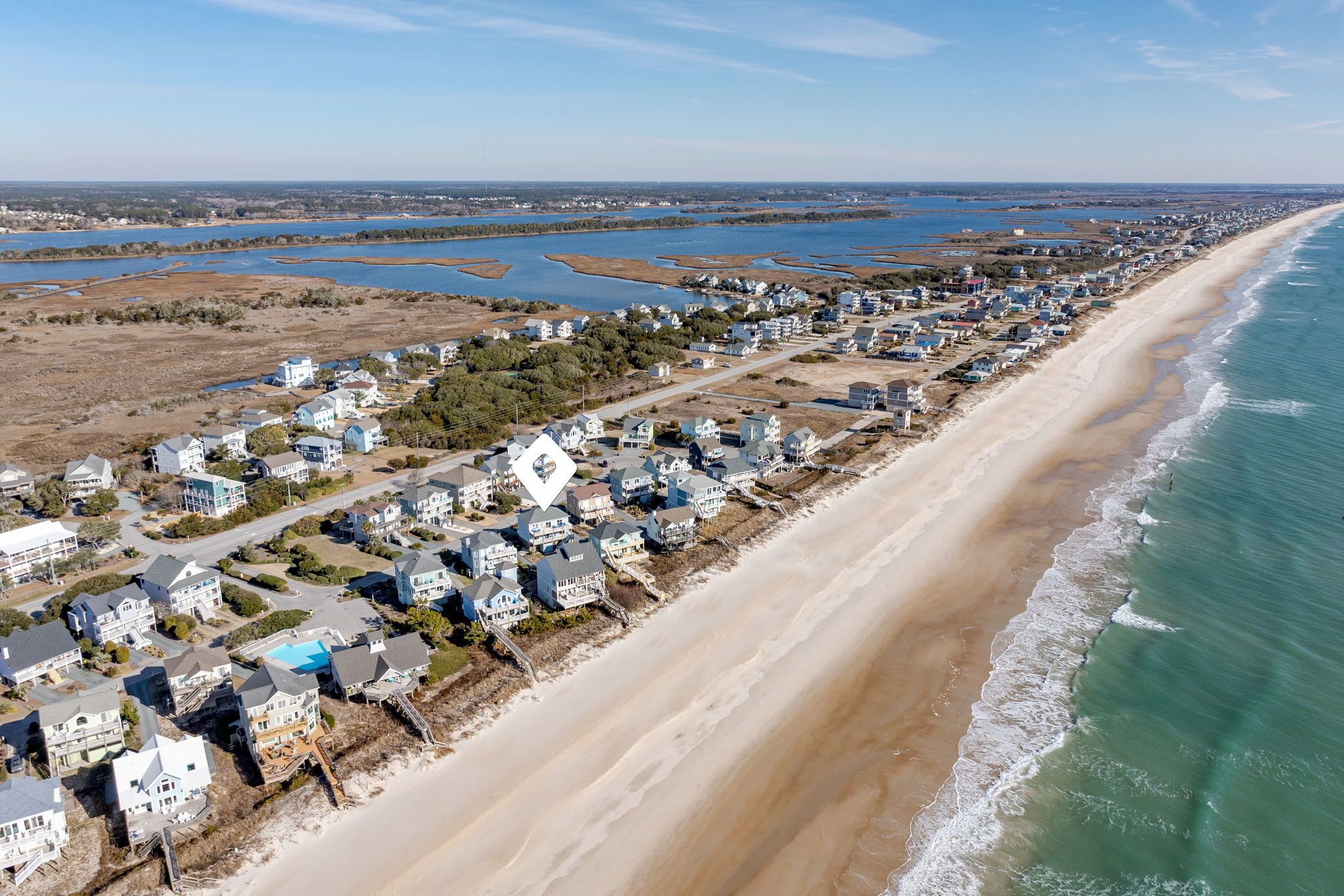 Luchtbeeld van een kustgebied met woningen langs een zandstrand en een groot wateroppervlak.