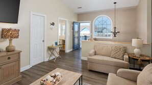 A spacious living room with a large window, a flat-screen TV mounted on the wall, and a cozy seating area with a sofa and armchairs. - Oceanfront home w/ Backyard Beach Access! (North Topsail Beach)
