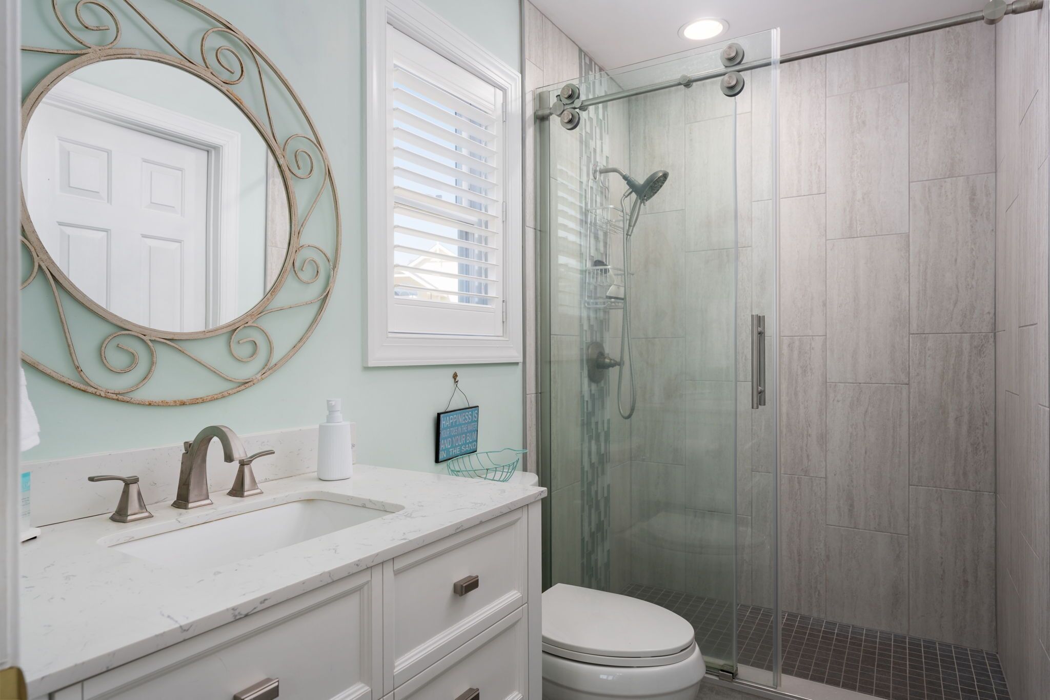 A bathroom with a white sink, a mirror with a decorative frame, a toilet, and a glass-enclosed shower.