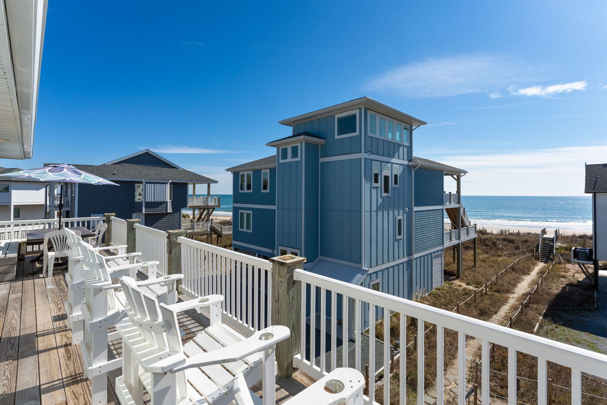A beachfront property with a deck, white chairs, and a blue building.
