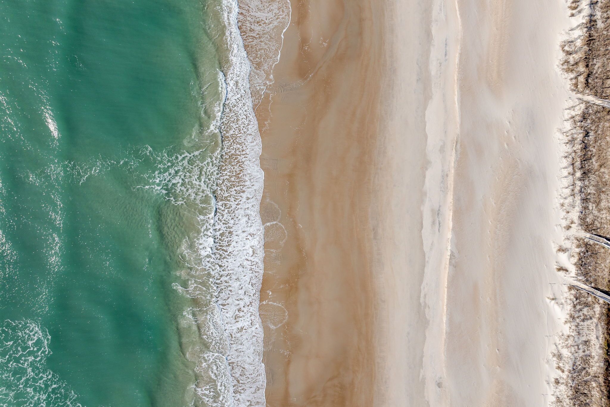 An aerial view of a beach with clear turquoise water and a wide sandy shore.