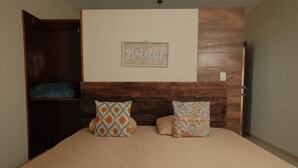 A bedroom with a wooden headboard, a bed with two patterned pillows, a wall-mounted artwork with the word "grateful," and a closet with a blue blanket. - Hanna suite  (Catemaco)