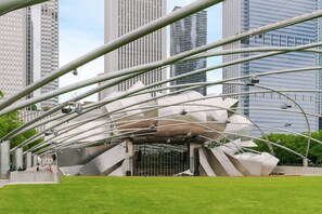 Une structure architecturale moderne, dotée d’un toit incurvé et d’une entrée centrale, entourée d’une pelouse et bordée, à l’arrière-plan, d’immeubles imposants.