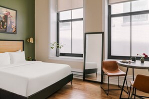 Une chambre d’hôtel avec un grand lit, une petite table avec des chaises, un vase de fleurs et un tableau au mur.