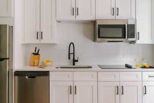 A modern kitchen with white cabinets, a stainless steel refrigerator, a microwave, a dishwasher, and a sink with a black faucet.