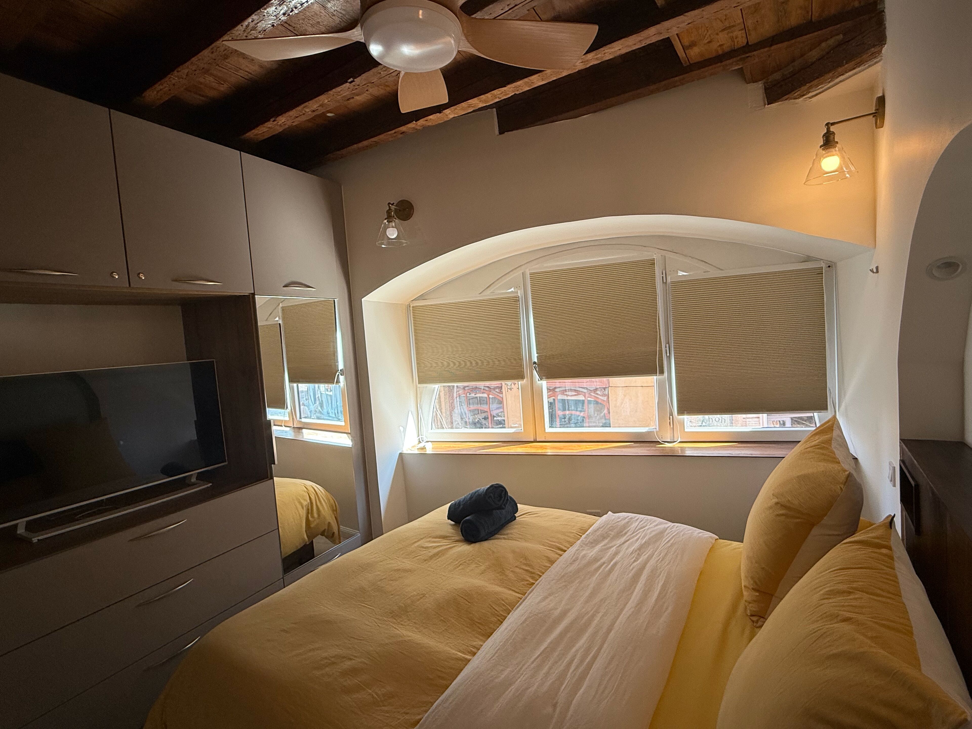 A bedroom with a bed, a television, and a window with blinds.